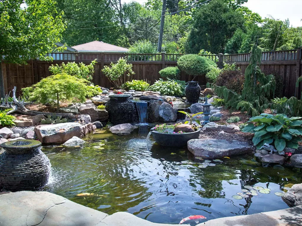 Backyard pond with cascading water features, decorative planters, and lush greenery in a private garden.