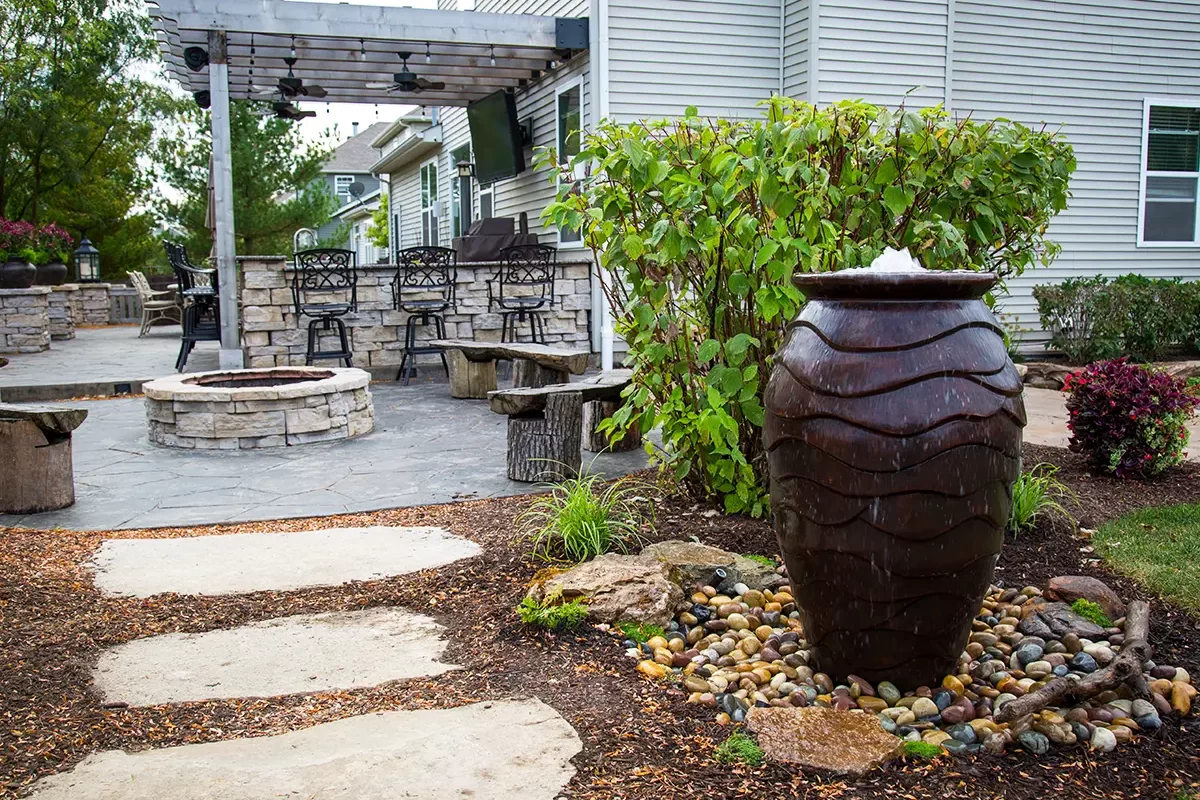 Backyard garden with large ceramic urn fountain and stone pathway leading to a seating area."